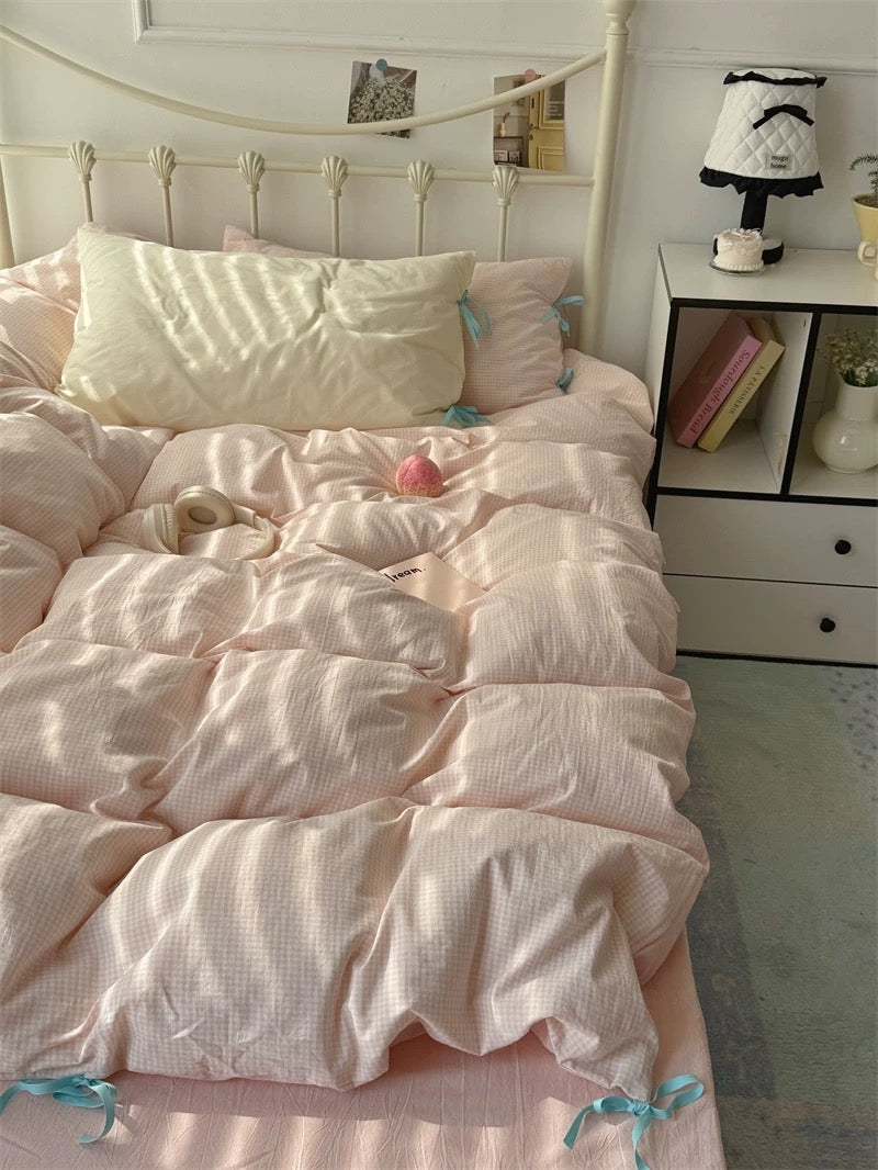 Bedroom with pink bedding and a nightstand with books and a lamp.