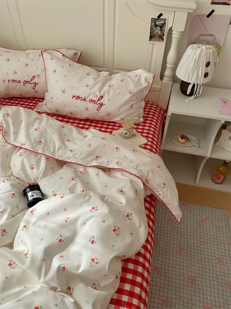 Bed with red and white checkered bedding and floral patterns, next to a nightstand.