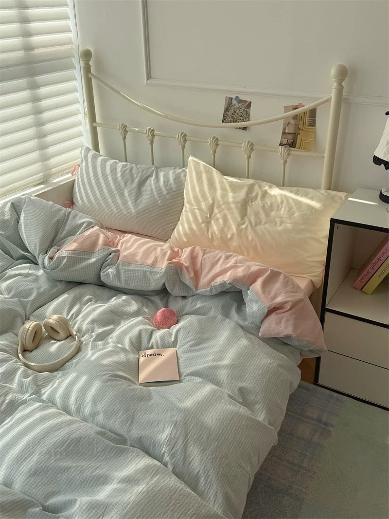 Bed with light-colored bedding and pillows in a room with a window and nightstand.