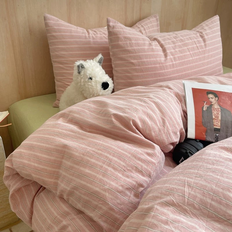 Bed with pink striped bedding, plush toy, and magazine on a wooden floor.