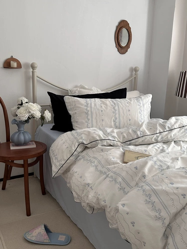 Bedroom with floral bedding and a side table with flowers.
