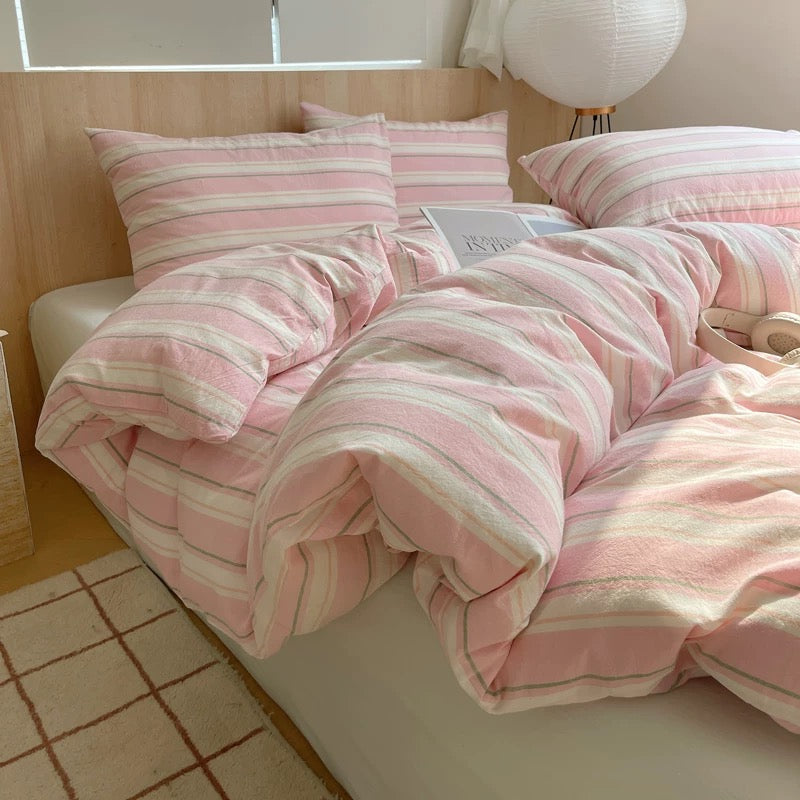 Pink and white striped bedding on a bed in a room with wooden flooring.