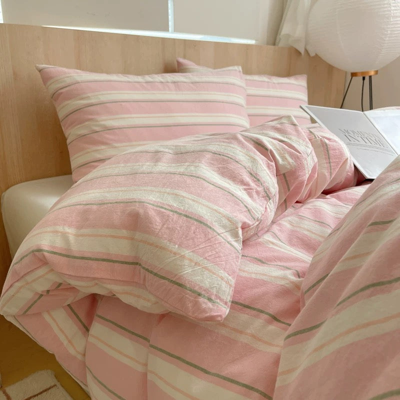 Pink and white striped bedding on a bed with a lamp in the background