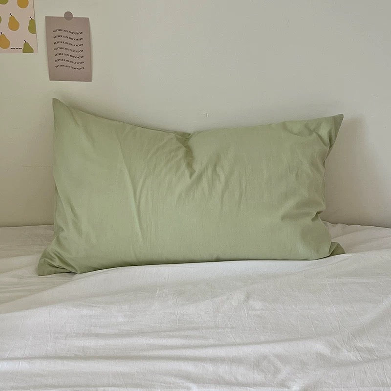 Plain soft sage green washed cotton pillowcase arranged on white bedding.