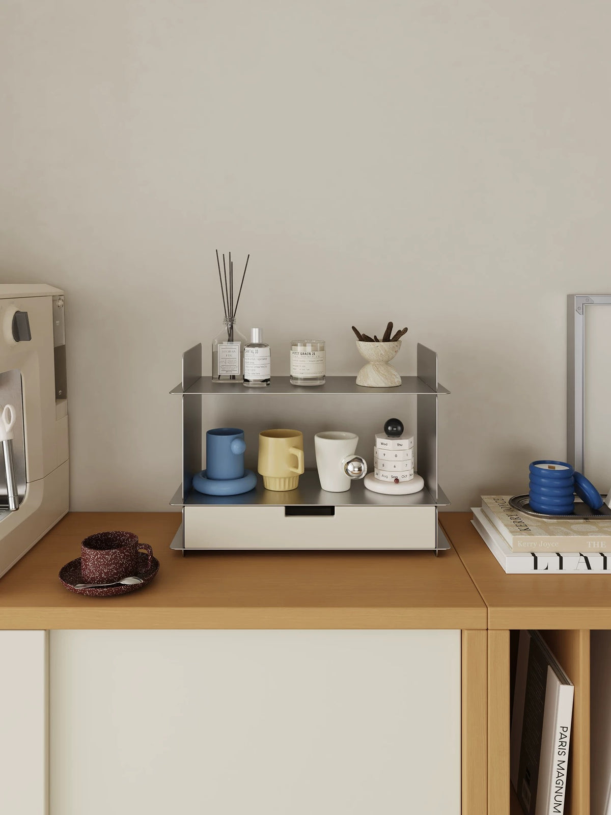 White stainless steel desk shelf with a drawer holding a reed diffuser, perfume bottles, a candle and three mugs