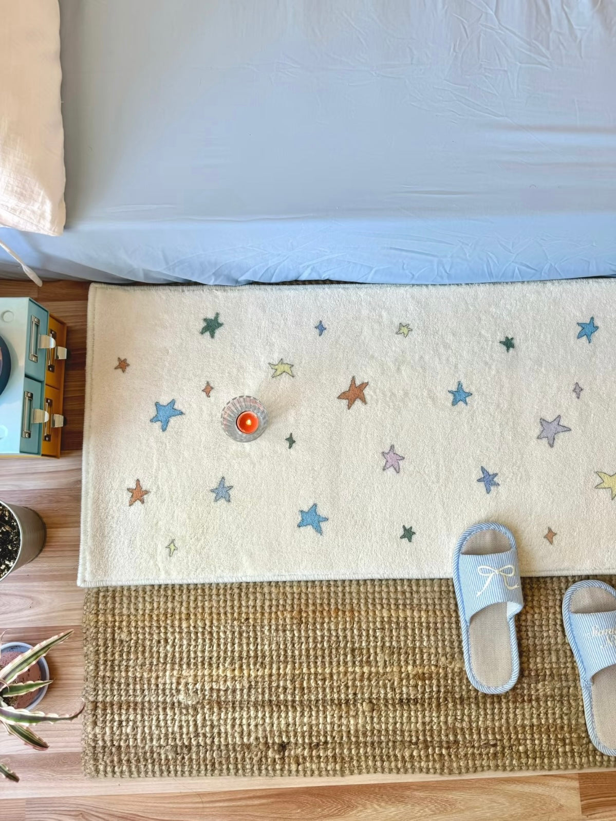 A star area rug with multicolor motifs lies flat beside a blue bed, with a glass near its center.