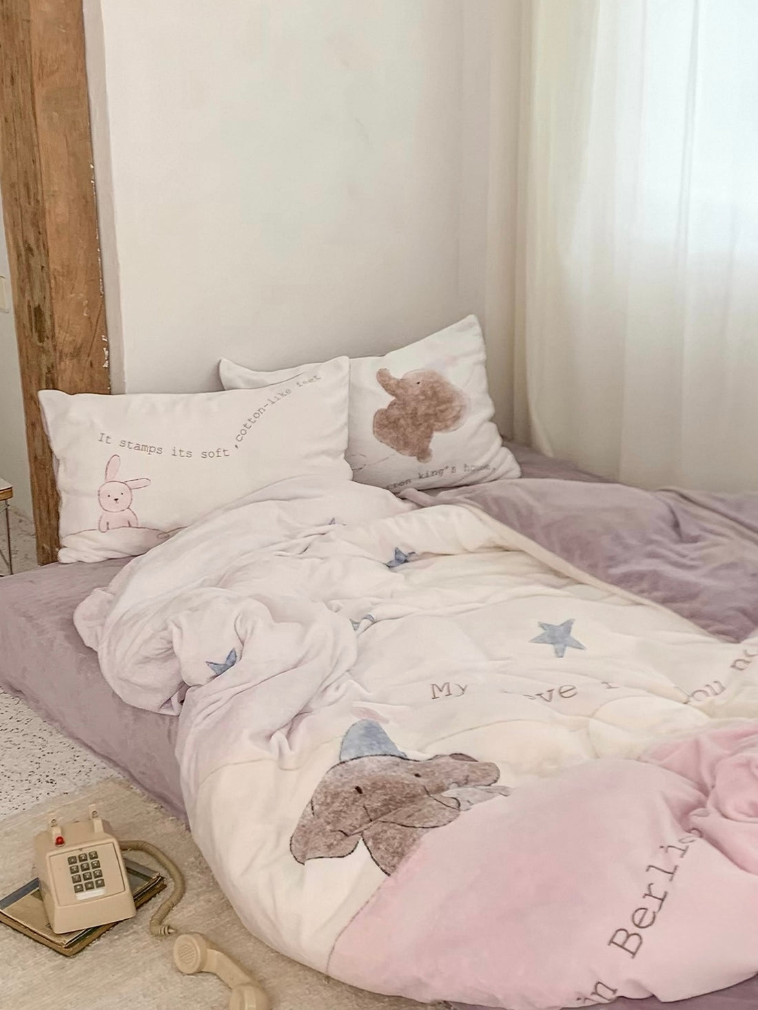 An elephant star duvet cover on a low bed has a cream center, pink border and purple sheet.