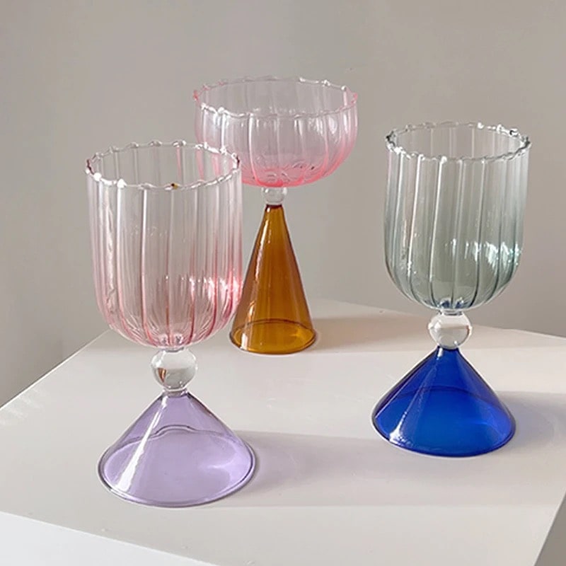 Colorful cocktail glass with gold rim, pink stem, and clear bowl displayed against neutral background.
