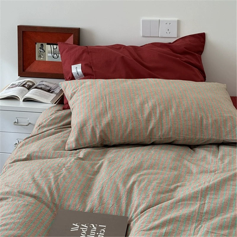 Bed with striped bedding and pillows, featuring a book and framed picture on the nightstand.