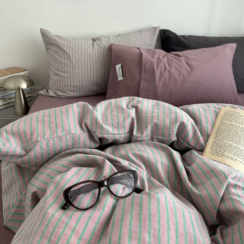 Bed with pink and green striped bedding, glasses, and a book on a white background