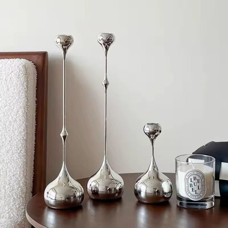 Set of silver vases on a wooden surface with a candle in the background