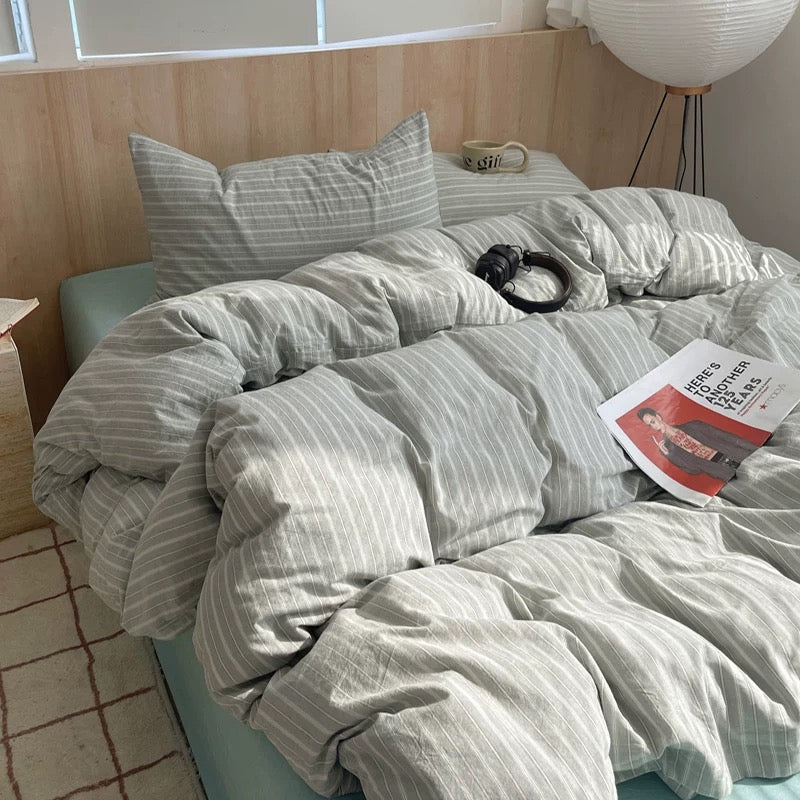 Bed with striped bedding and a cat, with a magazine on top, in a room with wooden walls and a light fixture.