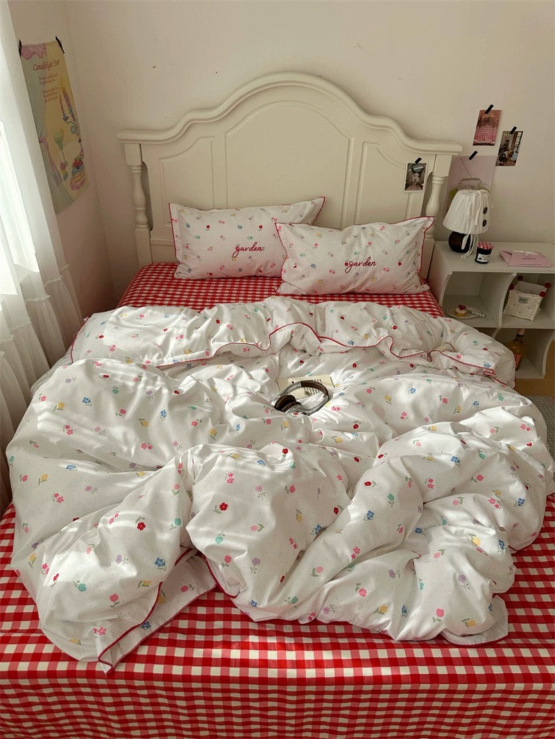 White floral-patterned comforter and pillows on a red checkered bedspread in a bedroom.