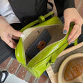 Person opening a green handbag on a brick surface