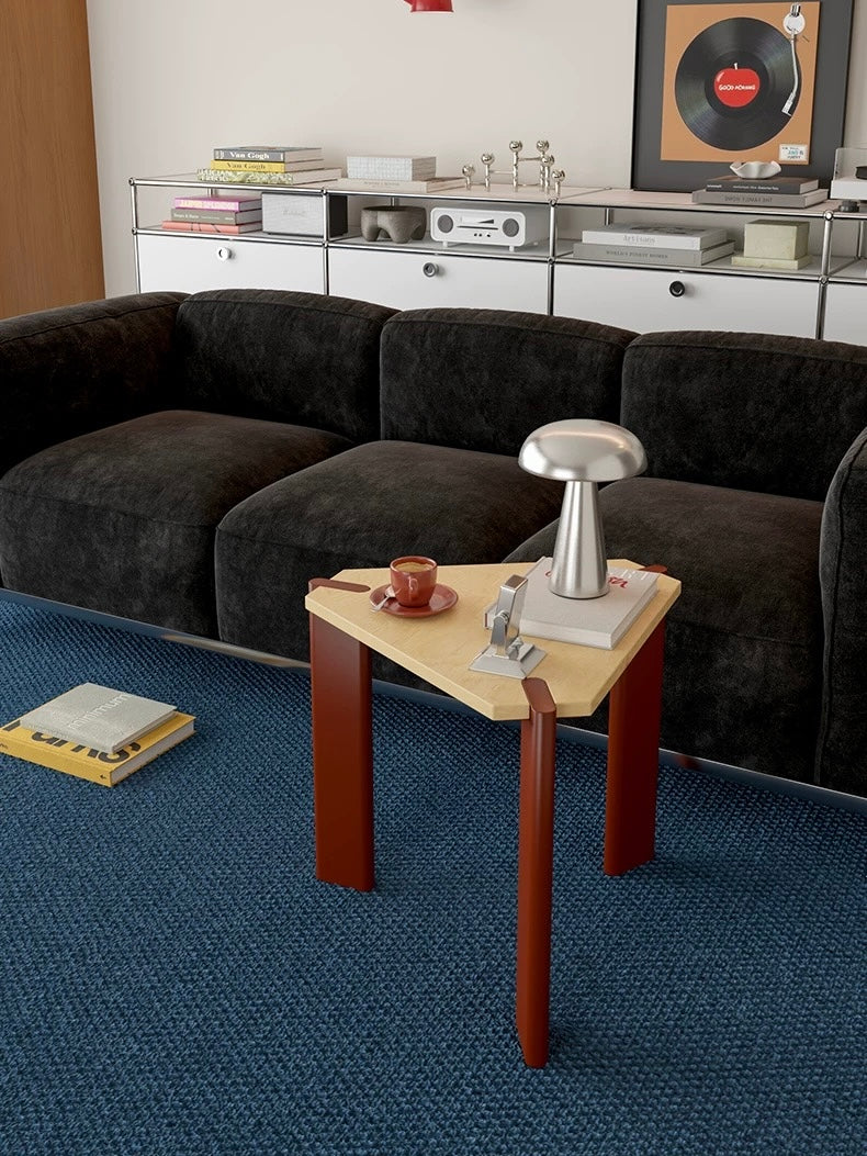 Triangle side table with burgundy legs and a natural wood top holding a silver lamp and a red cup.