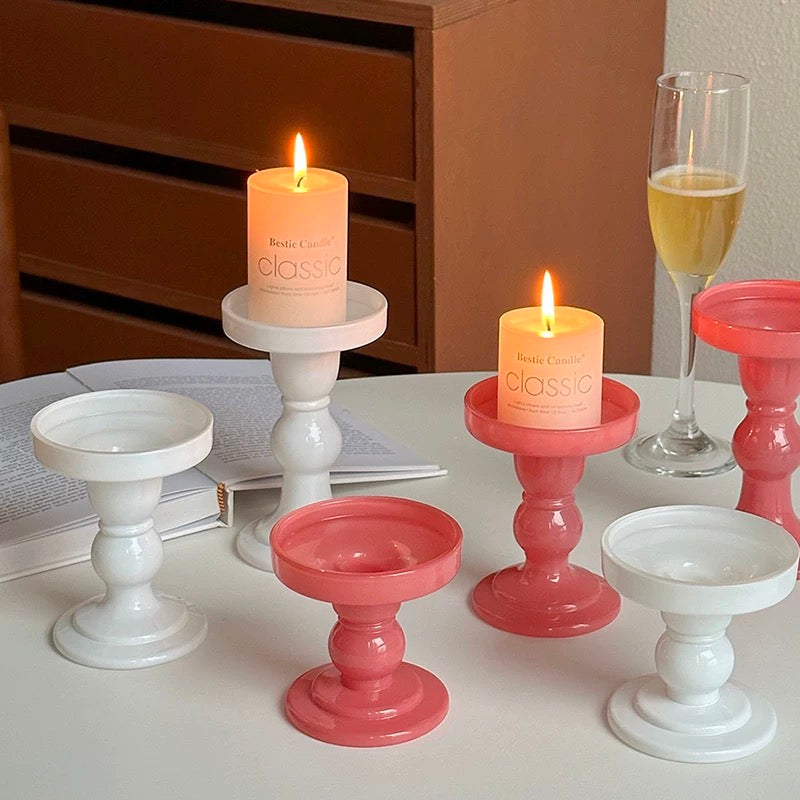 Set of small candle holders in pink and white on a table with lit candles.