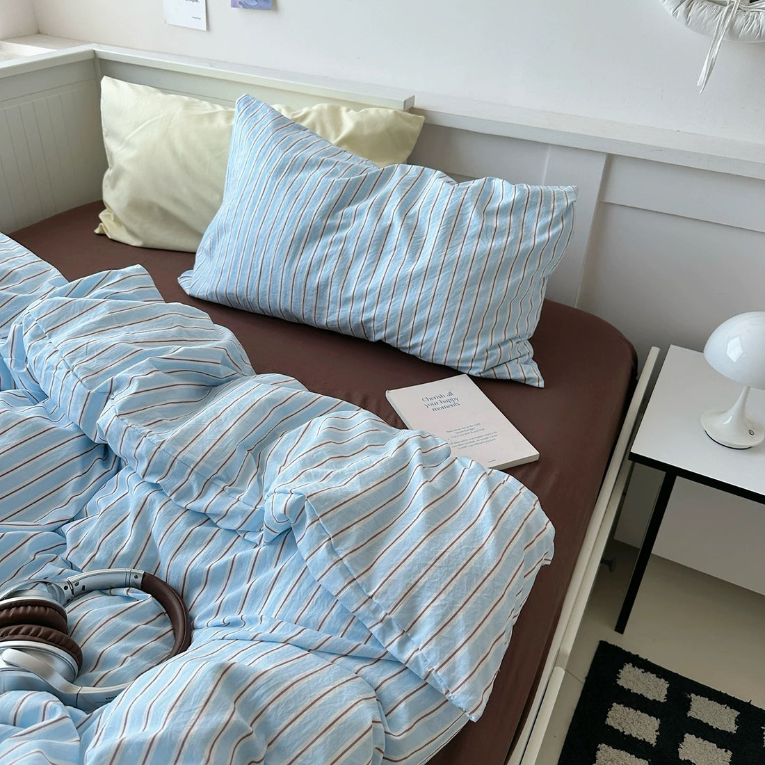 Bed with blue striped bedding and pillows, nightstand with lamp in the background