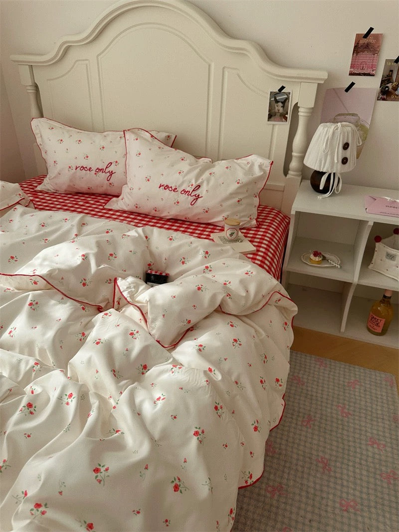 Bedroom with white floral bedding and red accents, featuring a nightstand with a lamp.
