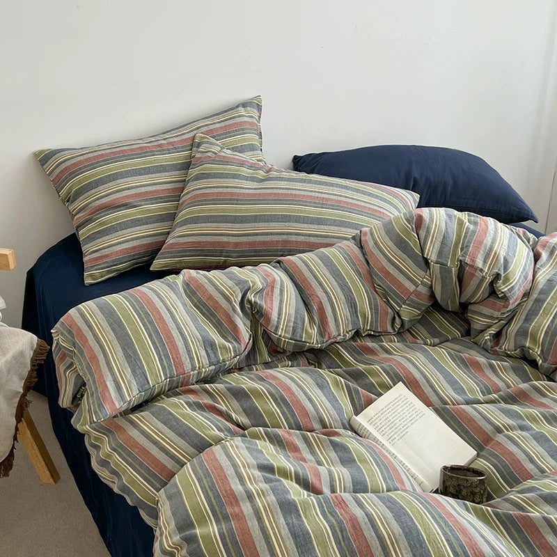 A bed dressed in a striped duvet cover and matching pillowcases with blue pillows, styled in a bedroom setting with a book on the duvet.