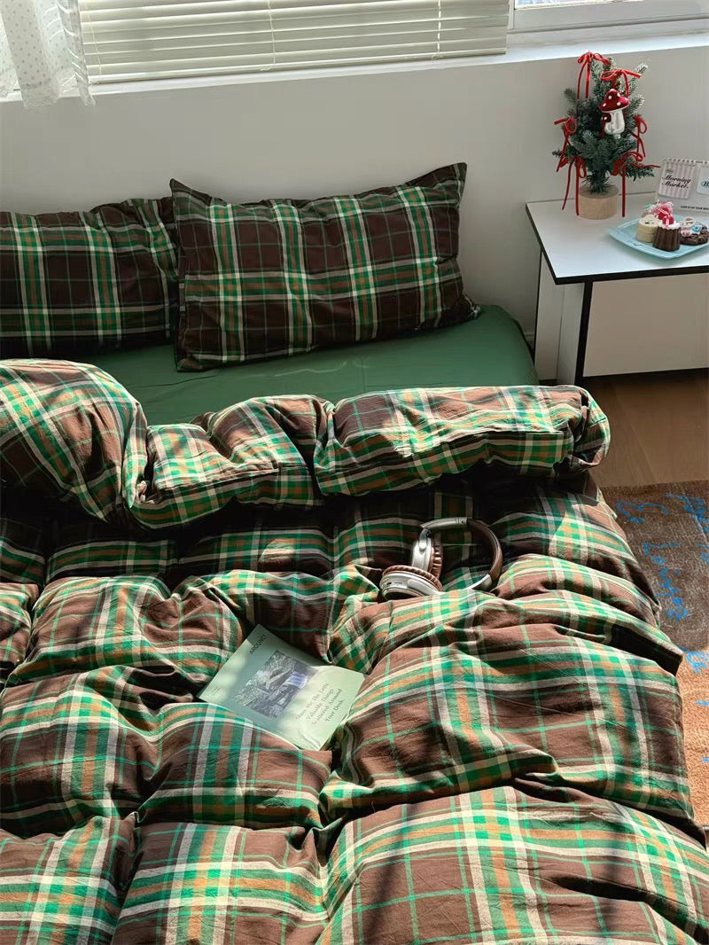 Plaid blanket on a bed with pillows and a small Christmas tree in the corner.