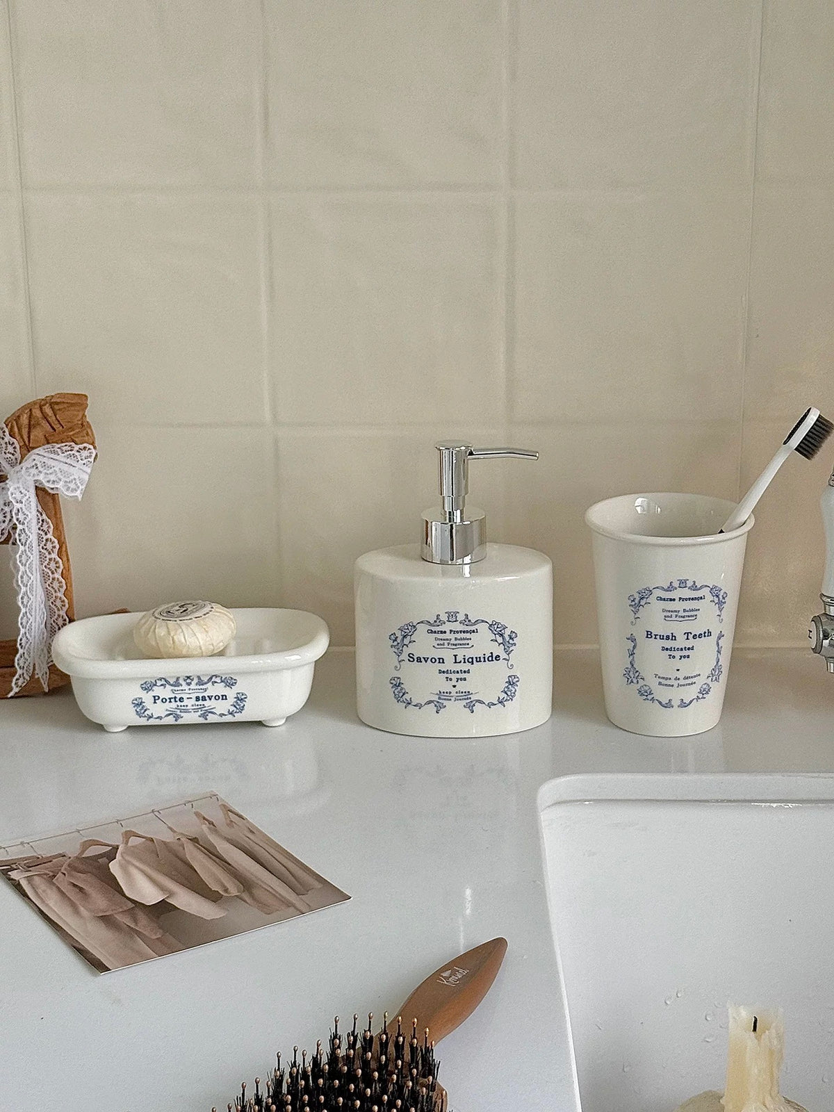 A vintage soap dispenser with blue floral lettering stands between a matching soap dish and toothbrush cup.
