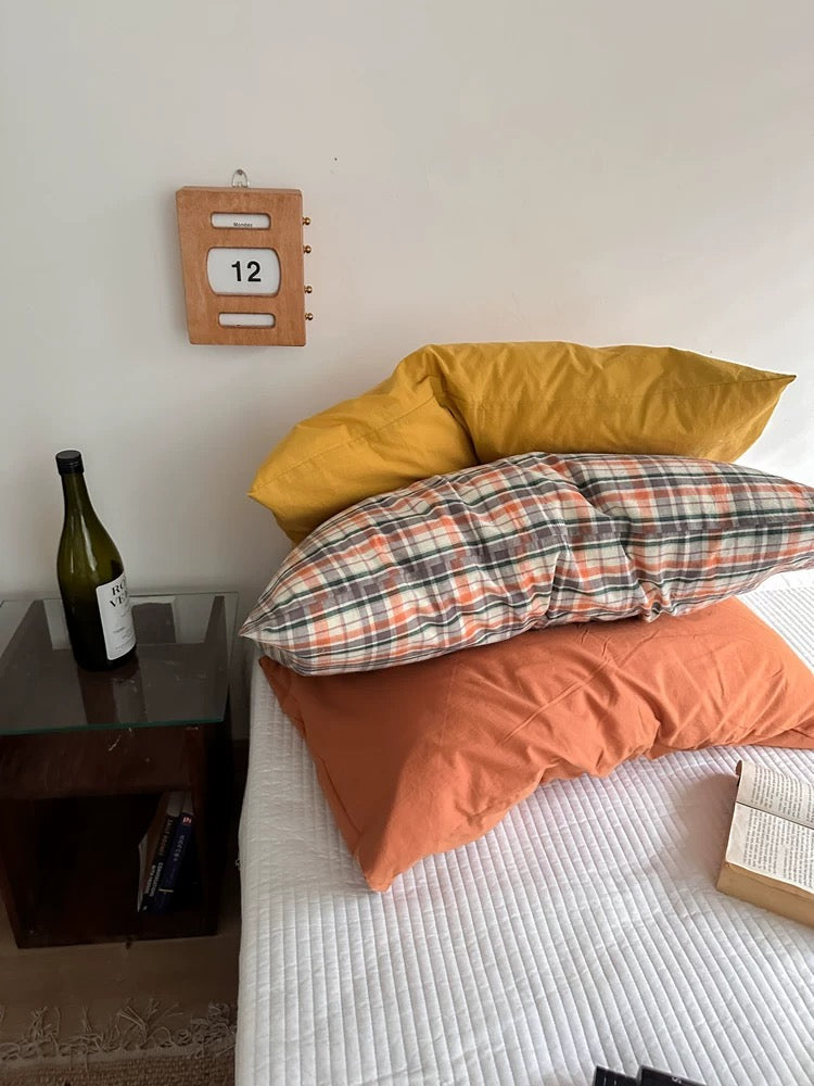 Mustard yellow, plaid and orange pillowcase designs are arranged across a white bed.