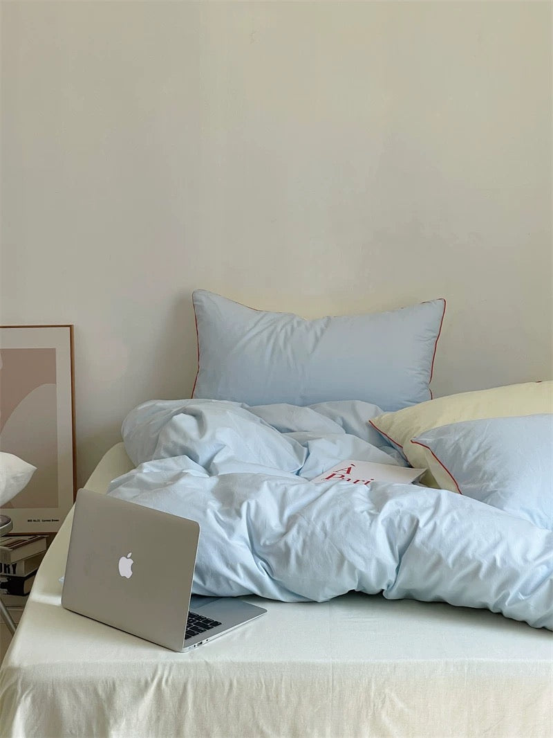 Laptop on a bed with a nightstand and window blinds in the background
