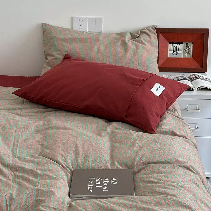 Red pillow on a bed with striped bedding and a framed picture in the background.