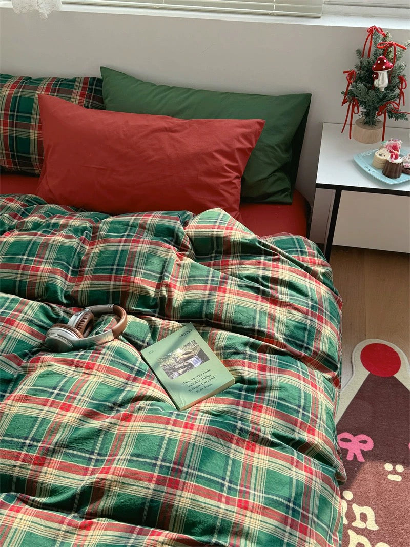 Bed with green and red plaid bedding, pillows, and a small Christmas tree on a nightstand.