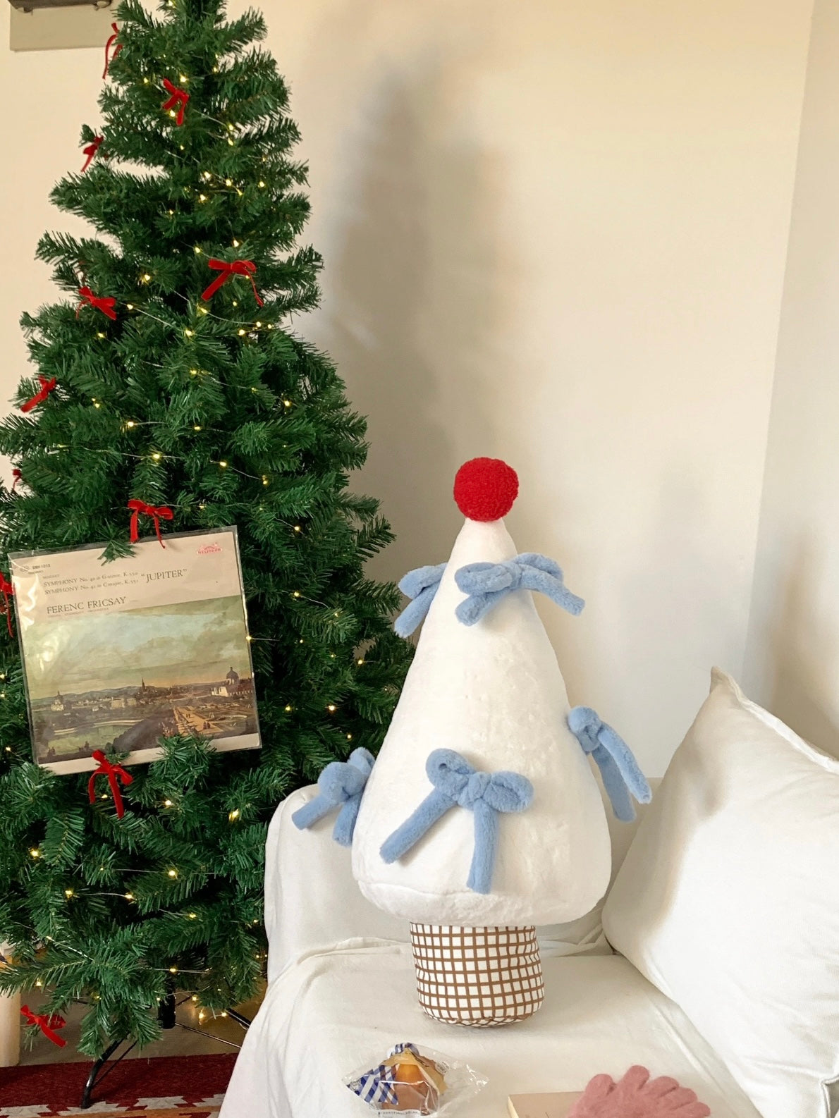 White Christmas tree pillow with blue bows styled beside holiday decor
