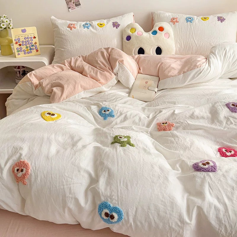 White cartoon embroidered duvet layered with pink bedding and matching embroidered pillows on the bed.