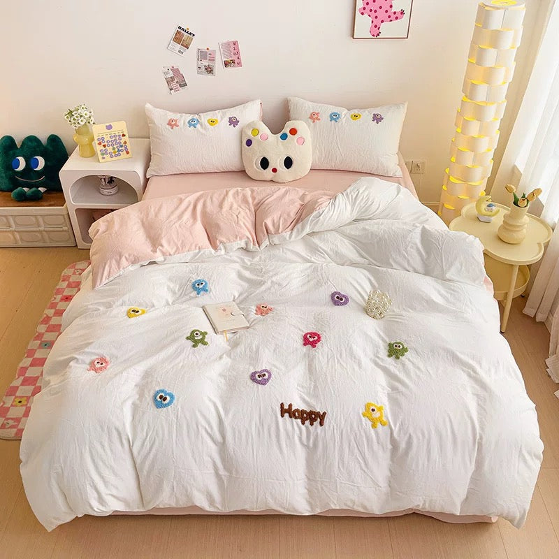 White duvet with colorful raised cartoon embroidery, matching embroidered pillowcases, and pale pink bedding layers.