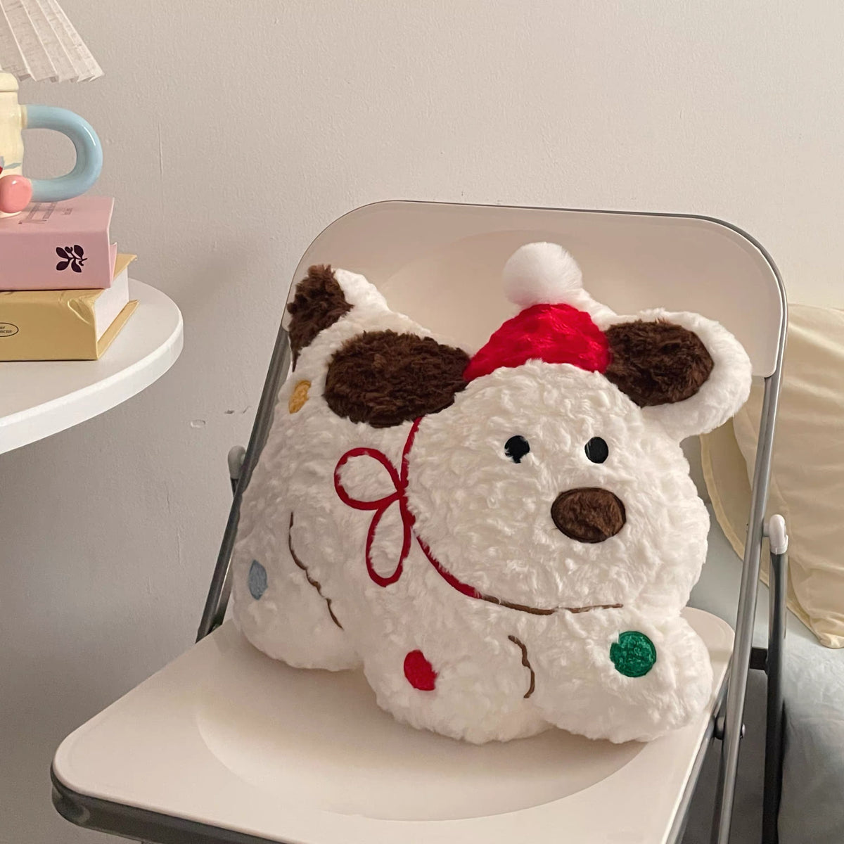 White Christmas dog throw pillow with red Santa hat on a white chair