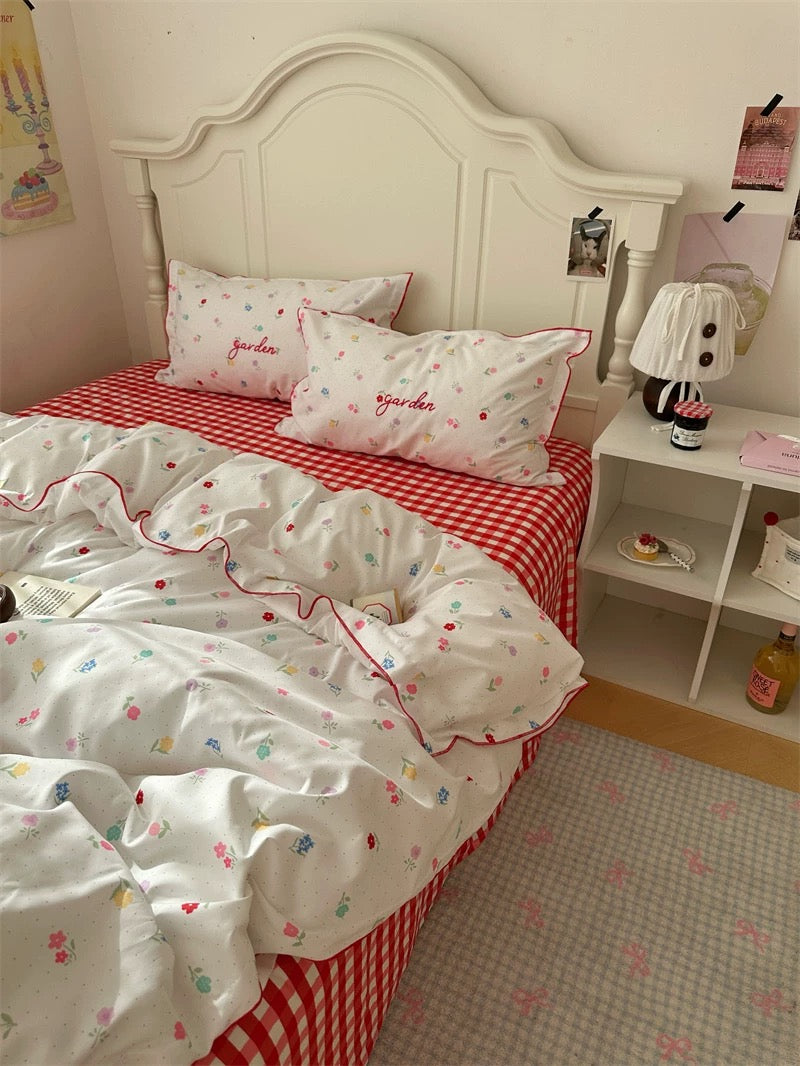 Bedroom with a bed featuring red and white checkered sheets and floral comforter, nightstand with lamp and decor items.