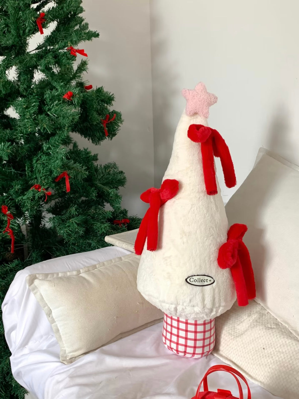 White and red Christmas tree pillow for couch styling beside a holiday tree