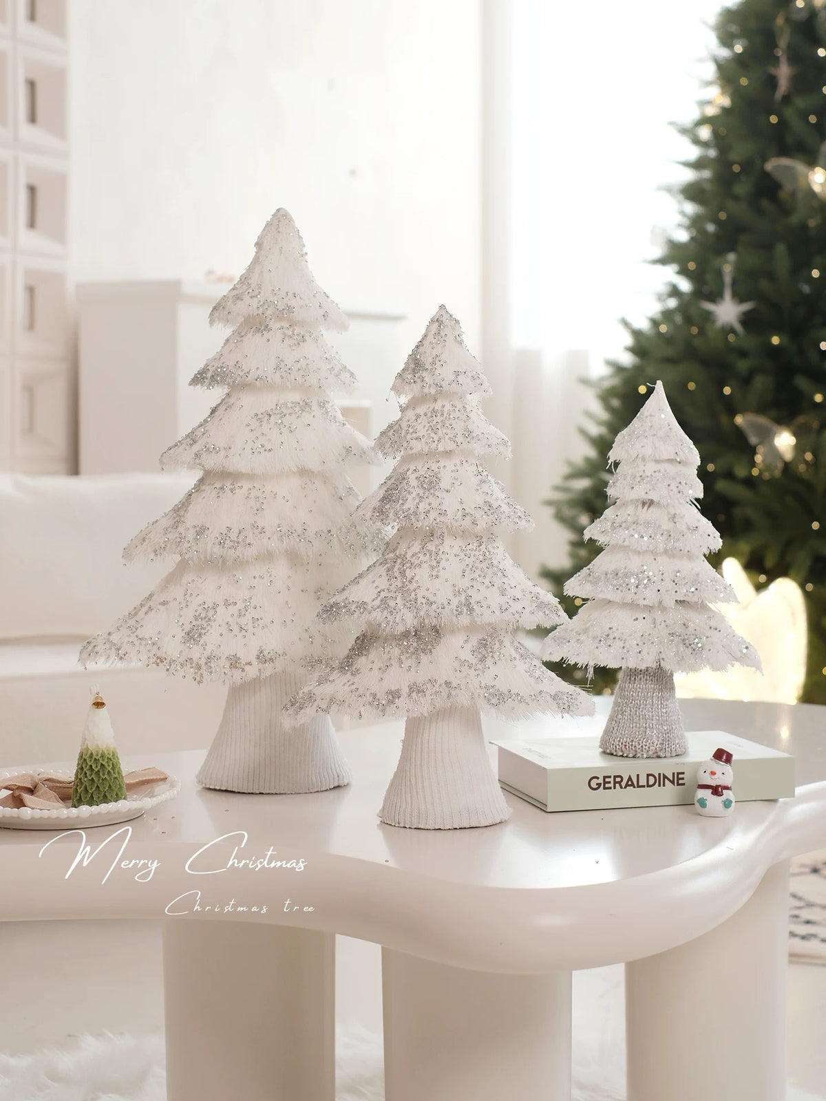White tabletop Christmas tree decorations stand together in a bright room, with their layered branches visible.