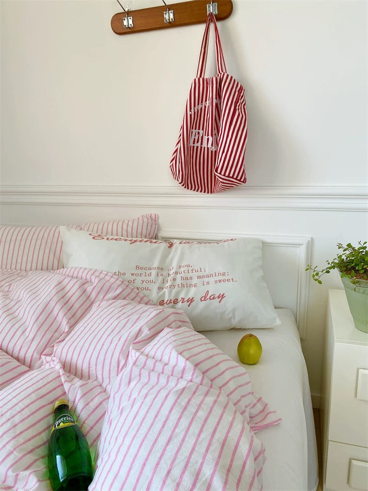 Bed with pink and white striped bedding, a bottle, and a green apple on a white nightstand.