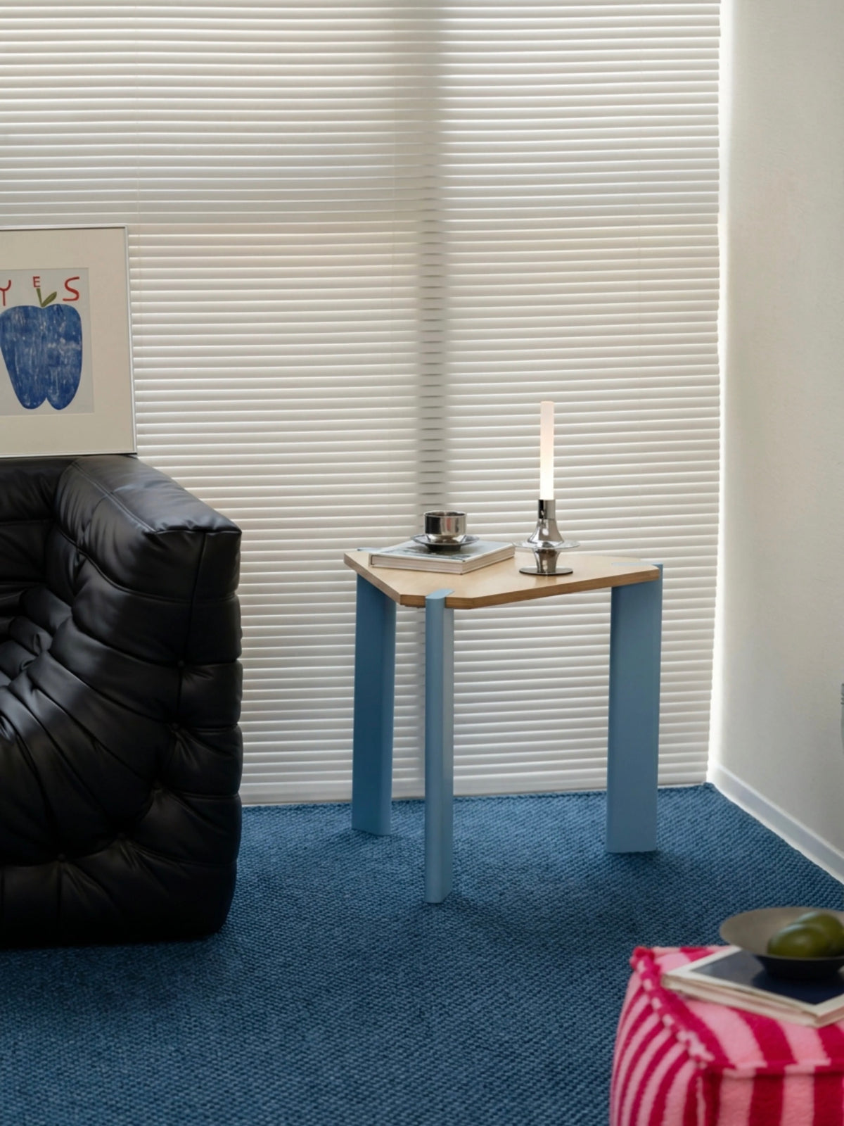 Wood and metal side table with pale legs and a triangular top holding small objects near a window.