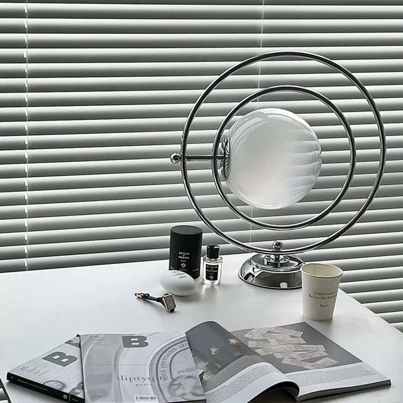 Table with a lamp, books, and a cup against a window with blinds