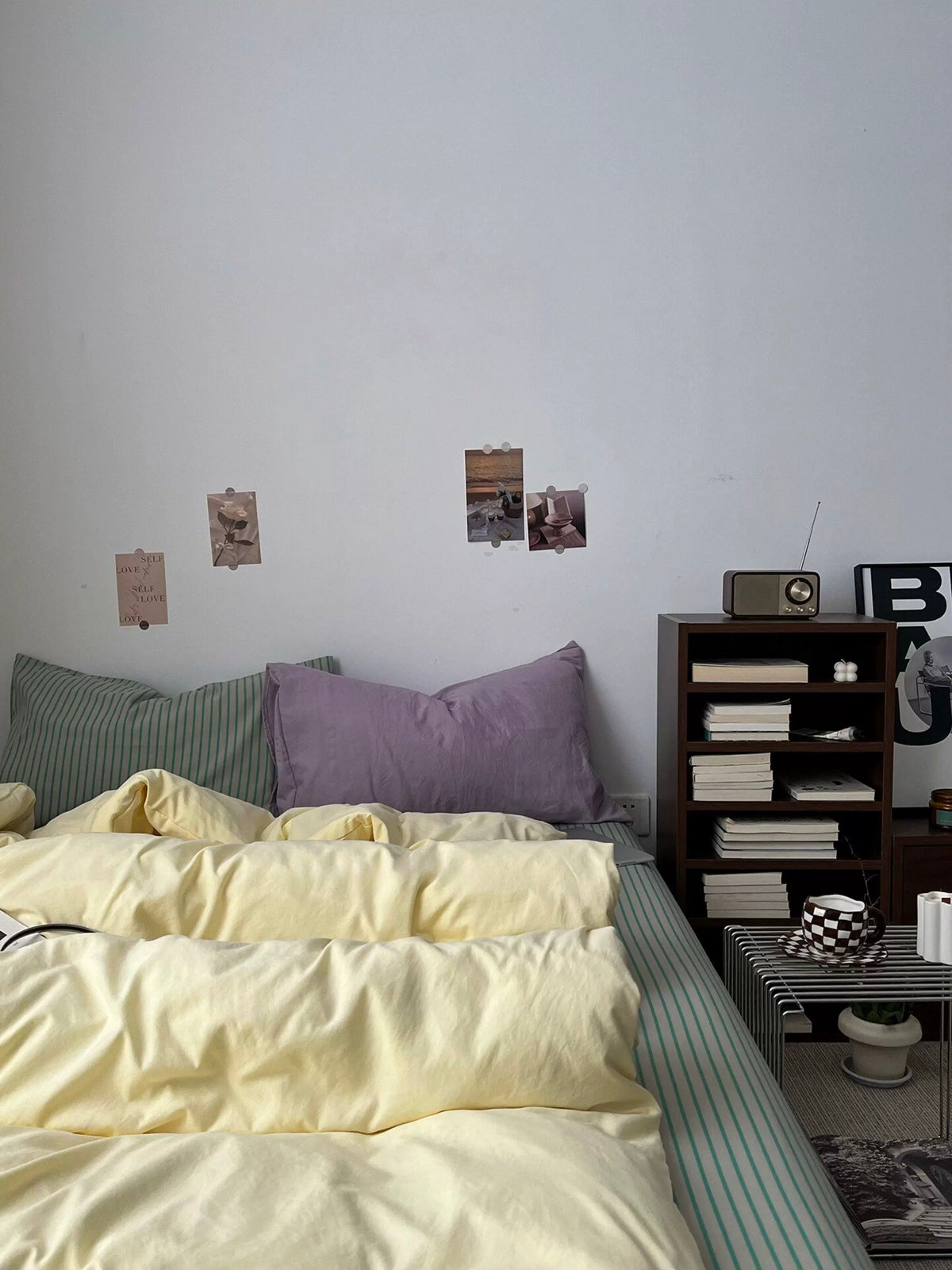 Butter yellow bedding with sage striped sheet and pillows against a white wall